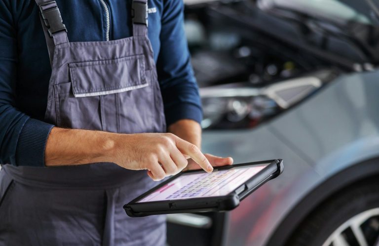 Mechaniker bedient ein Tablet zur Diagnose eines Fahrzeugs in einer Werkstatt.
