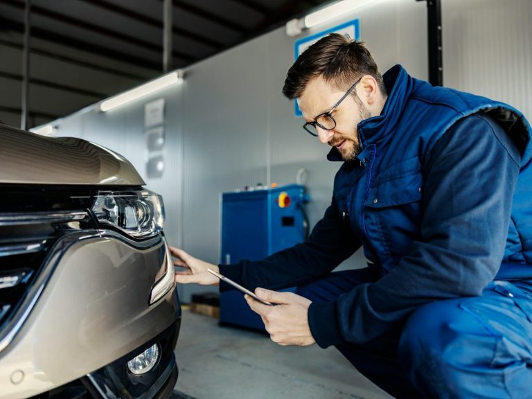 Ein Mechaniker überprüft den Scheinwerfer eines Fahrzeugs in einer Werkstatt.