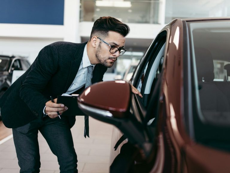 Mann in Anzug inspiziert einen roten Wagen in einem Autohaus.